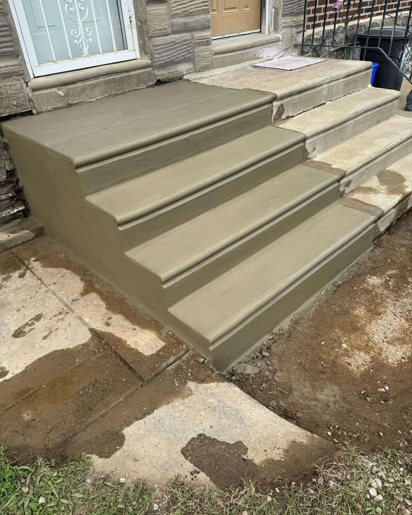 A set of freshly poured concrete steps leading to a house entrance, next to an older, weathered concrete staircase.