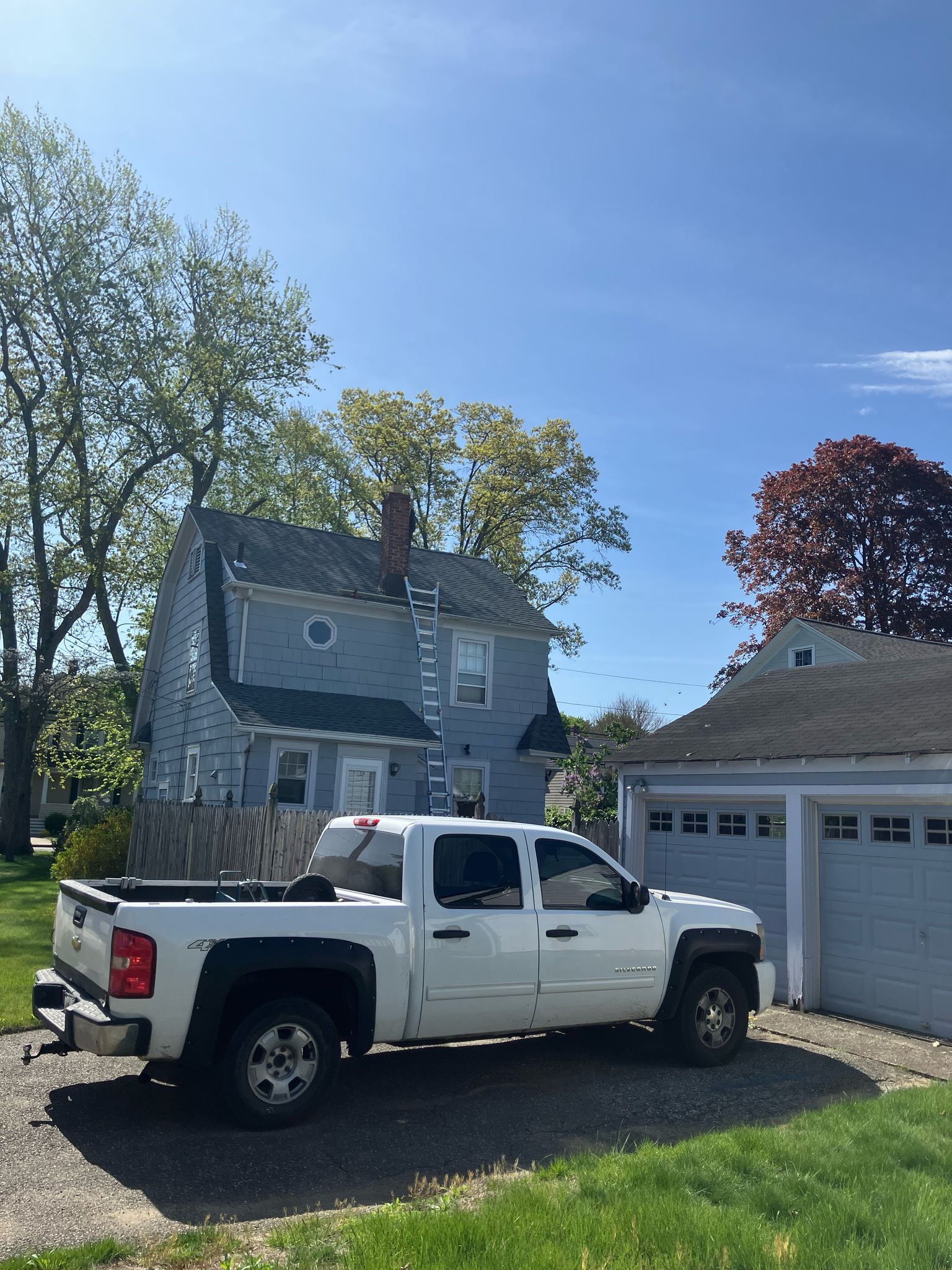 A white pickup truck is parked on a gravel driveway in front of a blue two-story house and a detached garage.