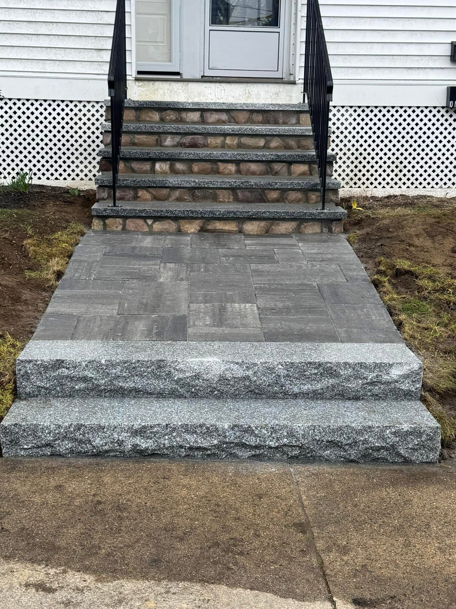 A front entrance with two granite steps leading to a paved landing, followed by four more steps to a white house door.