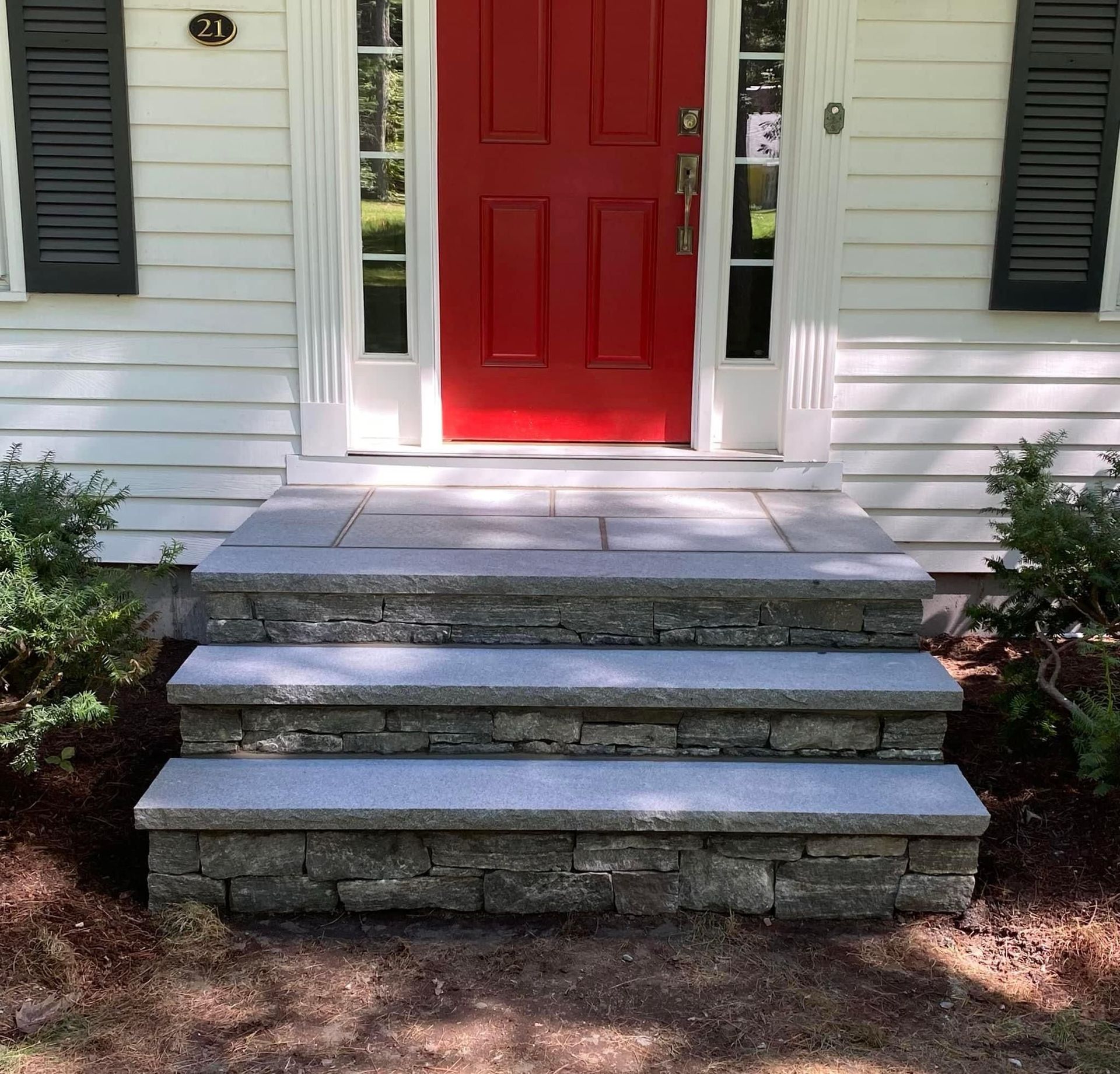 A vibrant red front door with white trim and black shutters above stone steps leading to a house entrance.