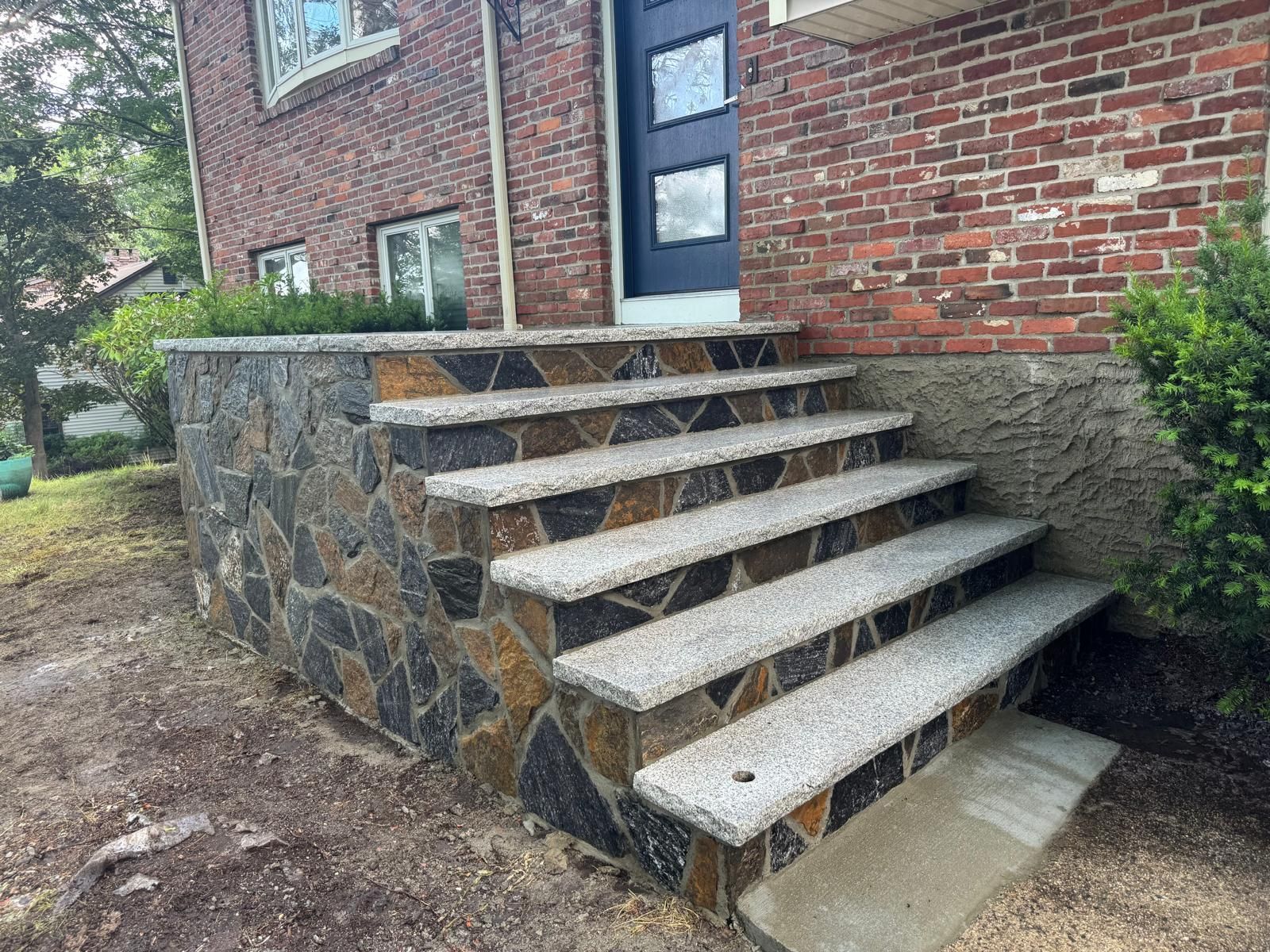 Stone-clad exterior staircase with four granite steps leading to a brick house with a blue door.