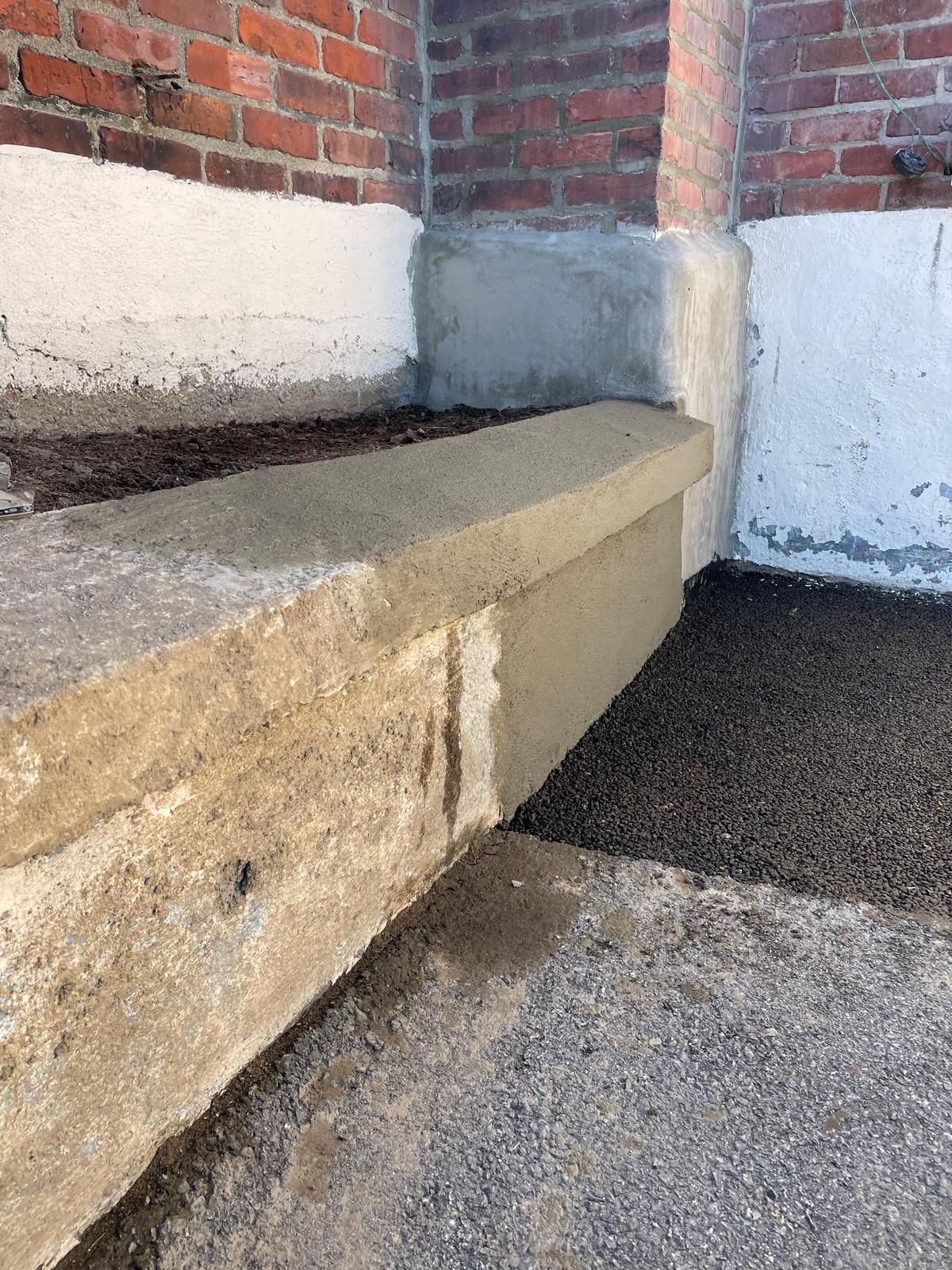 A concrete ledge being repaired with a patch of fresh mortar against a brick building exterior.