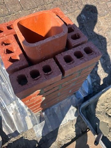A brick chimney stack under construction with a central clay flue liner, set against a paved surface.