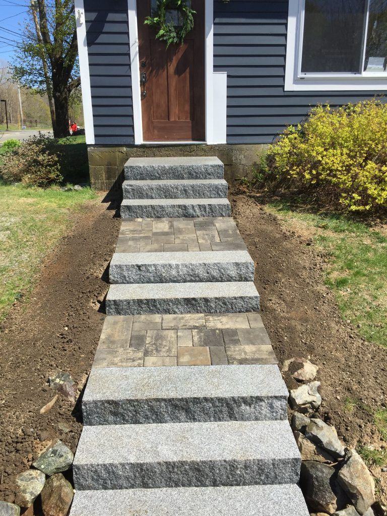 A walkway made of gray stone steps and pavers leading to the front door of a house with dark blue siding.