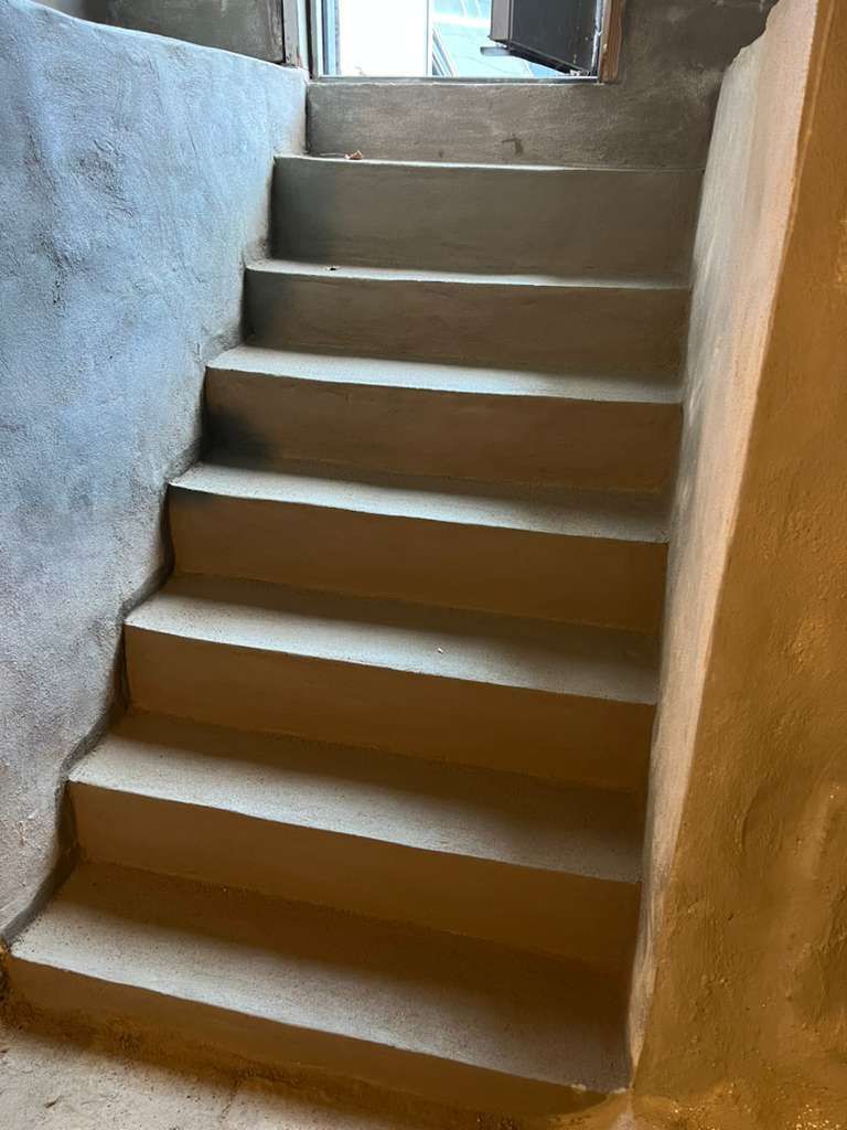 Narrow indoor staircase with unfinished concrete steps and walls, leading upward toward a doorway