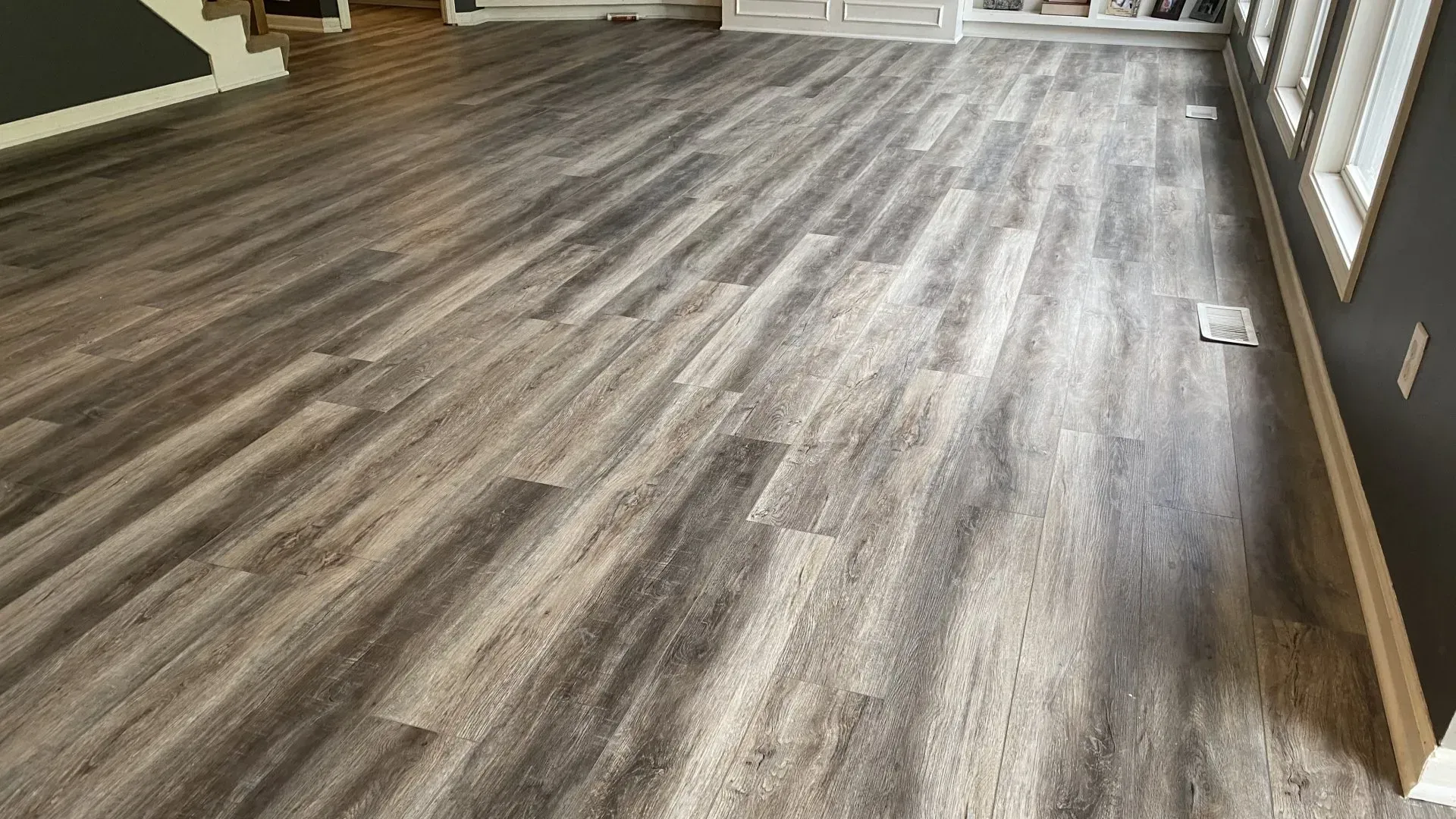Gray wood-look flooring extends across a room with a white baseboard and a dark gray wall.