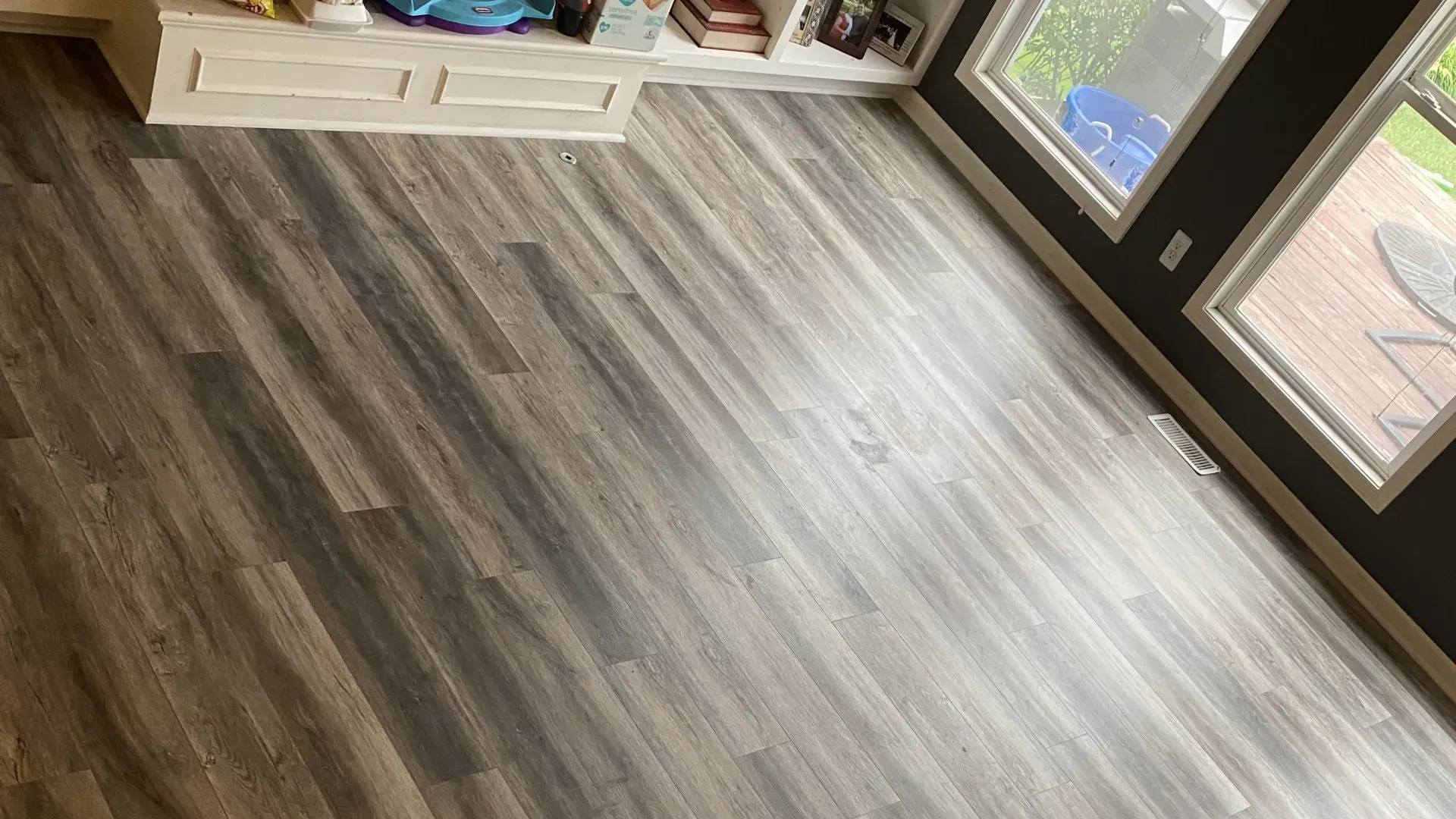 Wood-look flooring in a room with a built-in shelf and windows. Sunlight reflects off the planks.
