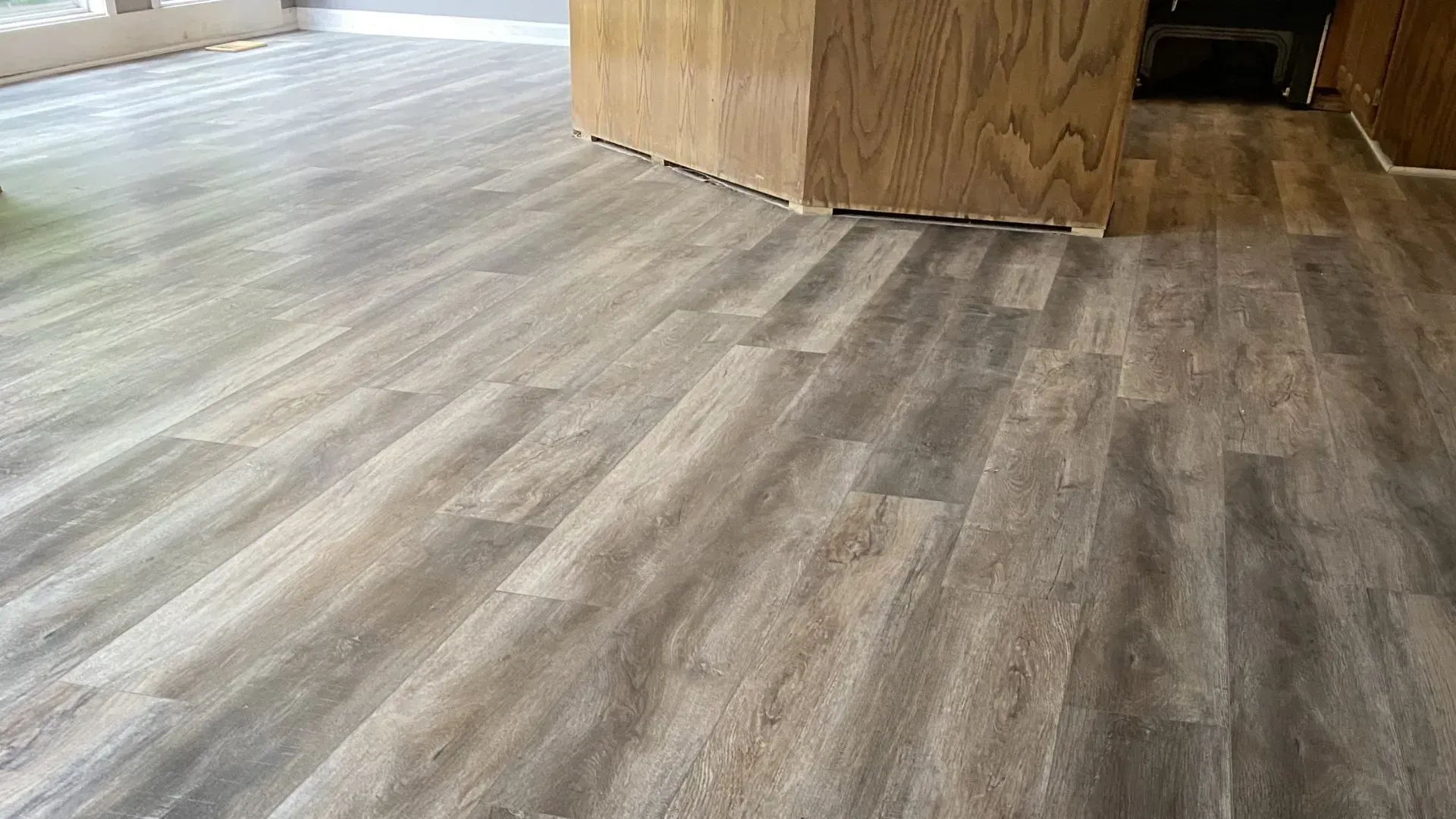 Wood-look flooring in shades of gray and beige, with a wooden cabinet visible in the background.
