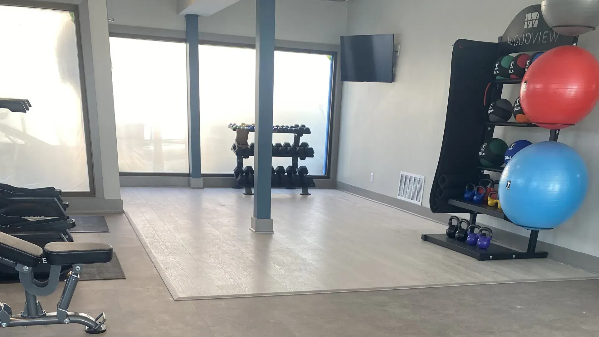 Home gym with weights, exercise balls, and a bench. Natural light streams in from the windows.