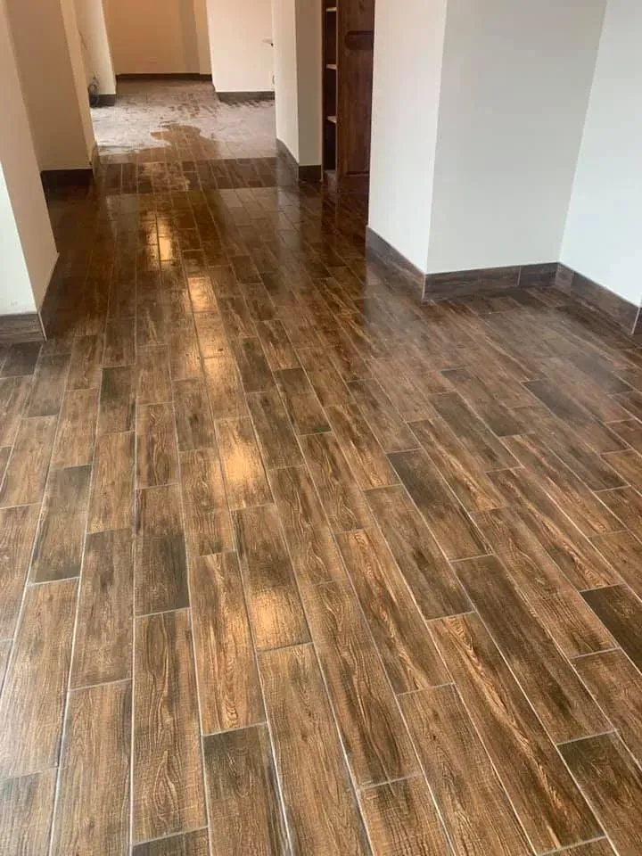 Brown wood-look tile floor in a hallway with white walls and dark trim.