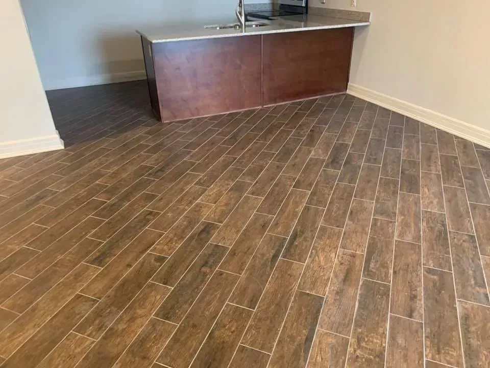Brown wood-look tile flooring in a room with a dark wood island and light walls.