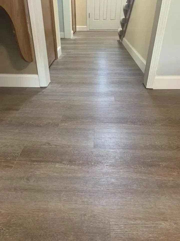 Hallway with wood-look flooring. White baseboards and door frames. A door and stairs are visible.