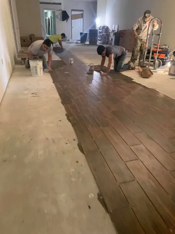 Workers installing wood flooring in a room. Men are on their knees applying adhesive to planks.