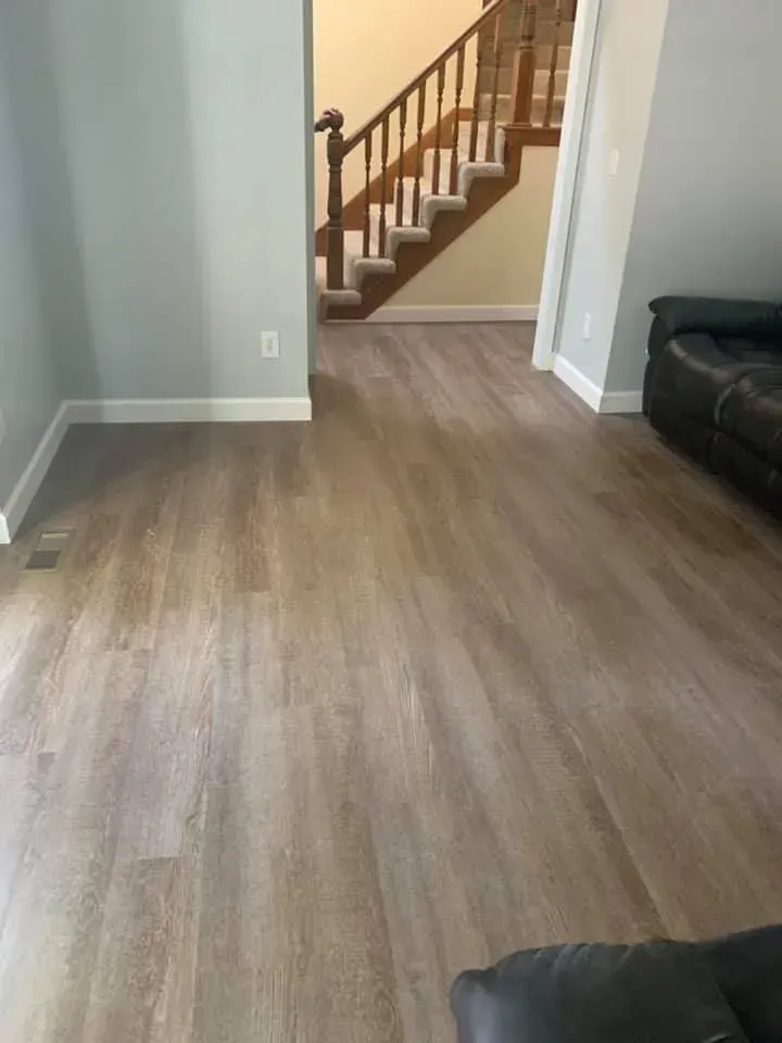 Living room with wood-look flooring and light blue walls. Stairs are visible in the background. A black couch is on the right.