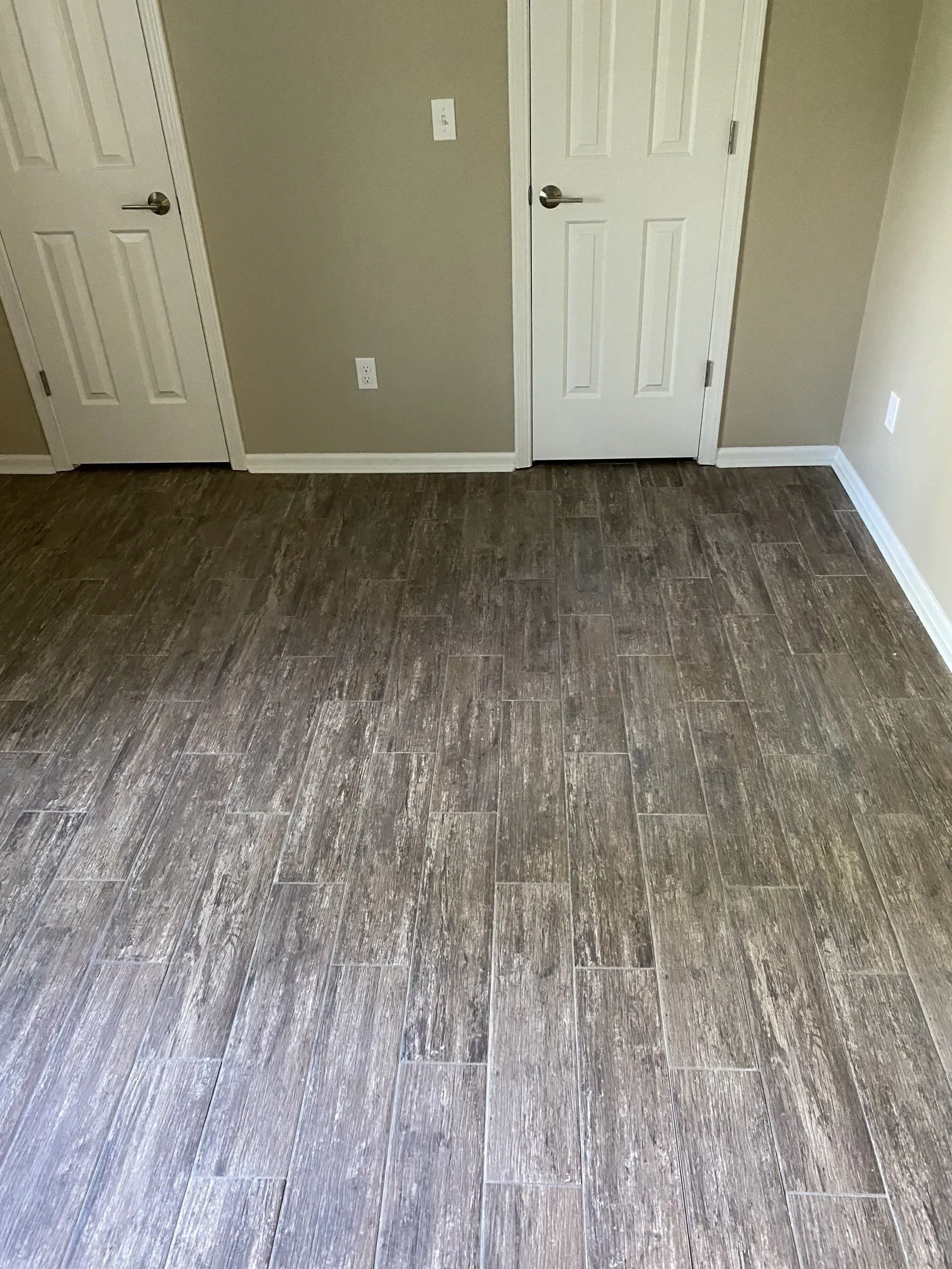 Room with wood-look flooring, two white doors, and beige walls.