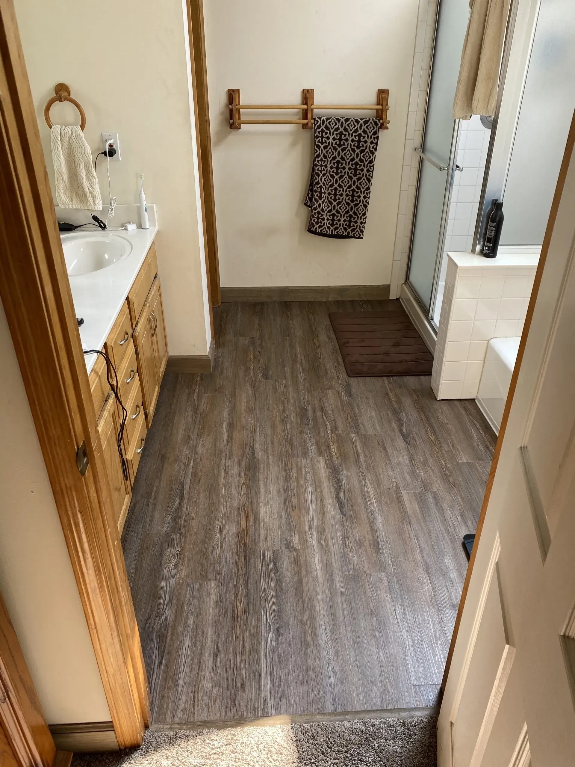 Bathroom with wood-look flooring, vanity, and shower. Towels hang on a rack.