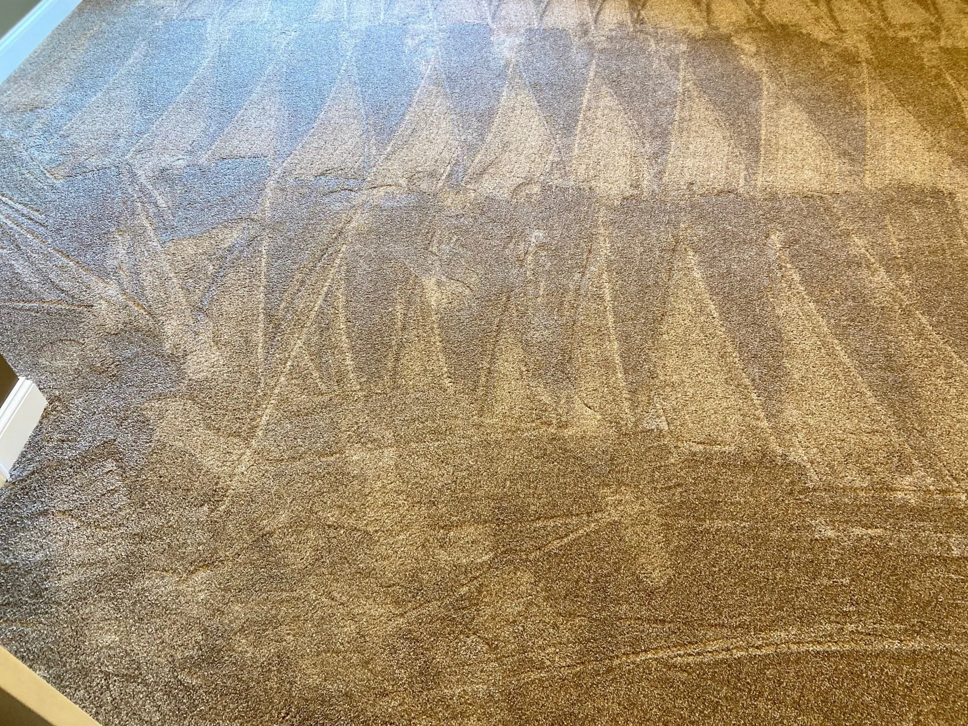 Cleaned brown carpet with triangular patterns, viewed from above, with a white wall on the left.