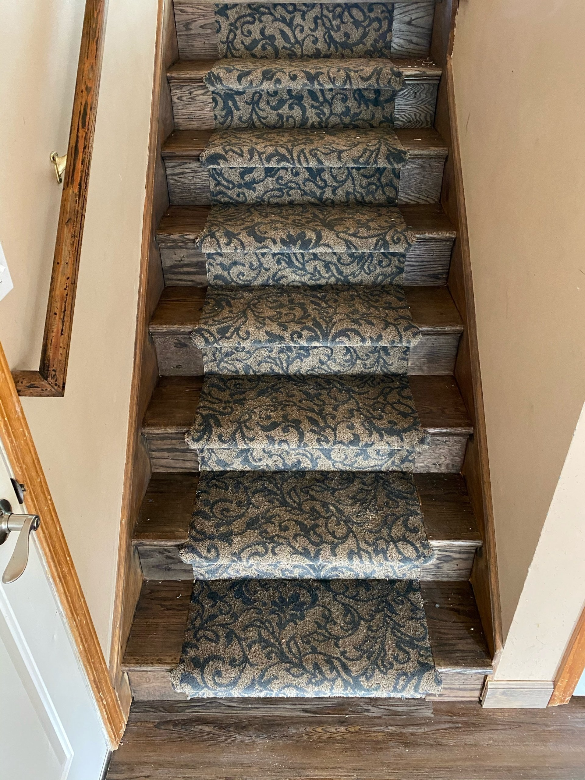 Staircase with floral pattern carpet runner; wooden steps and frames, neutral walls.