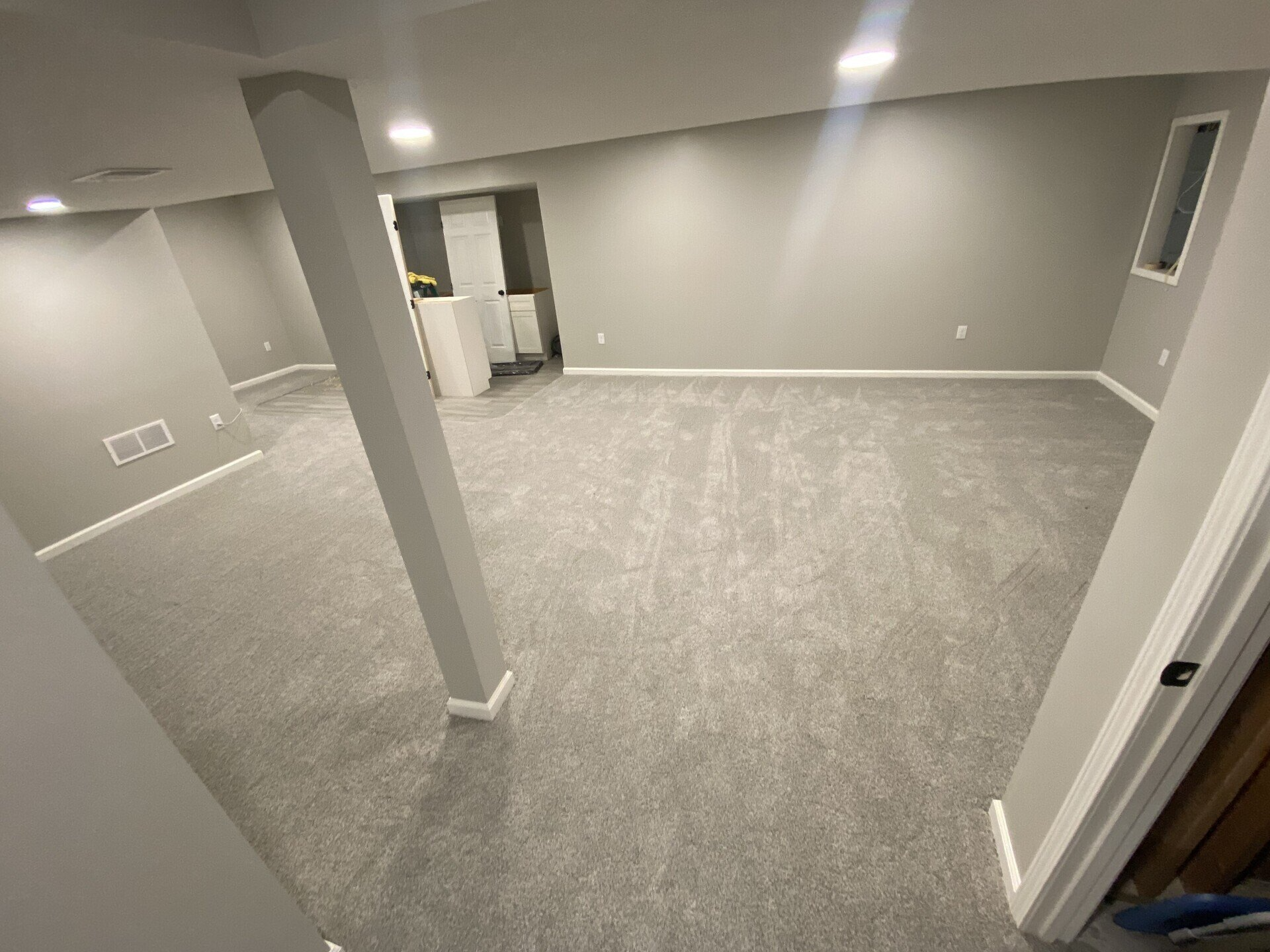 Empty basement room with gray carpet, walls, and support columns.