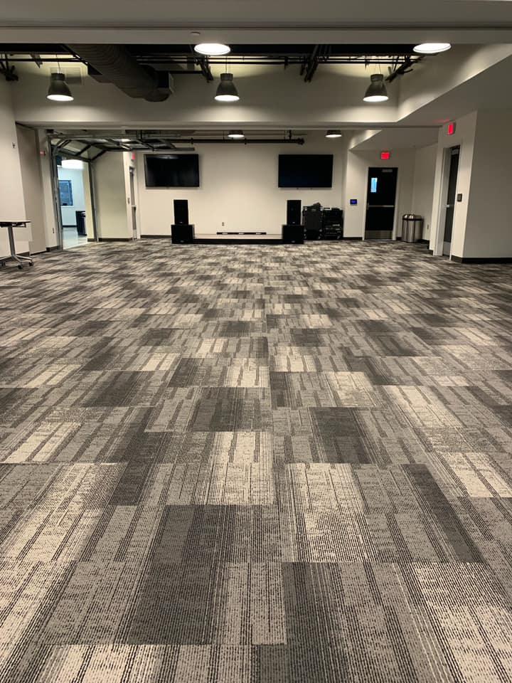 Empty event room with gray patterned carpet, speakers, and two mounted TVs.