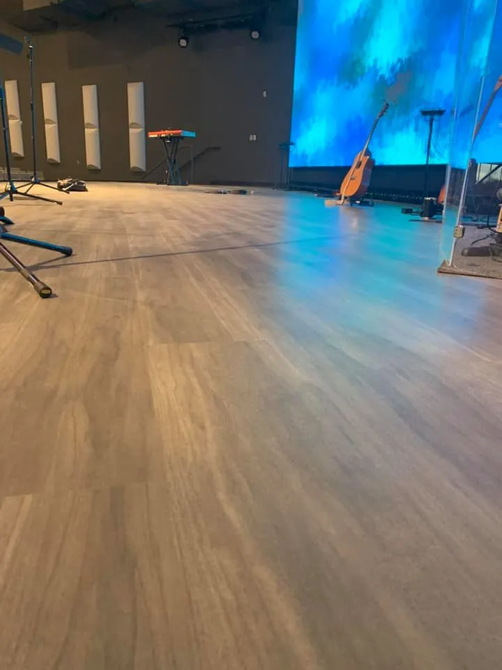 Wooden floor of a stage reflecting blue and green lights, with a guitar, microphone stands, and a stool.