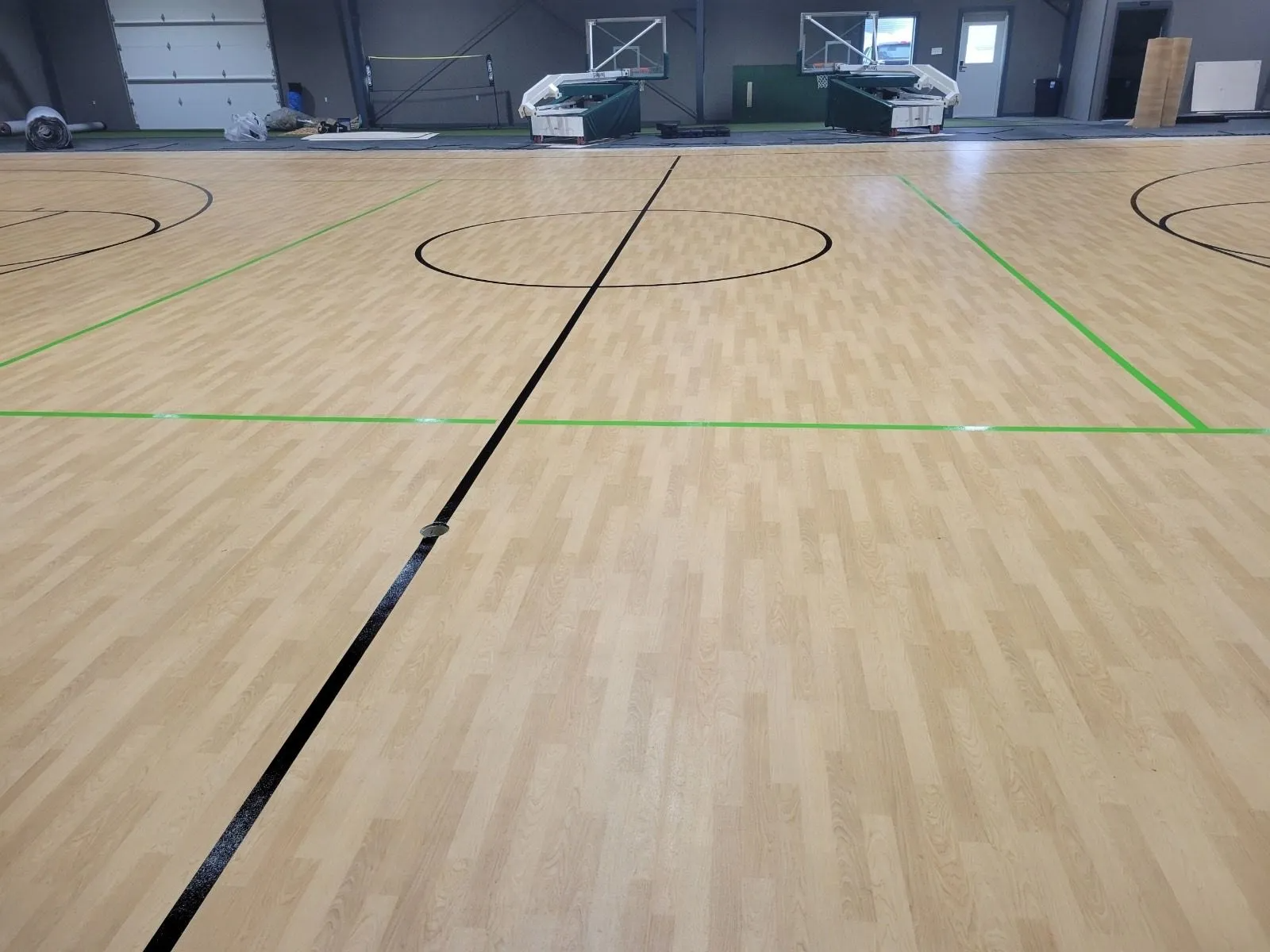 Basketball court with light wood flooring and black and green lines.