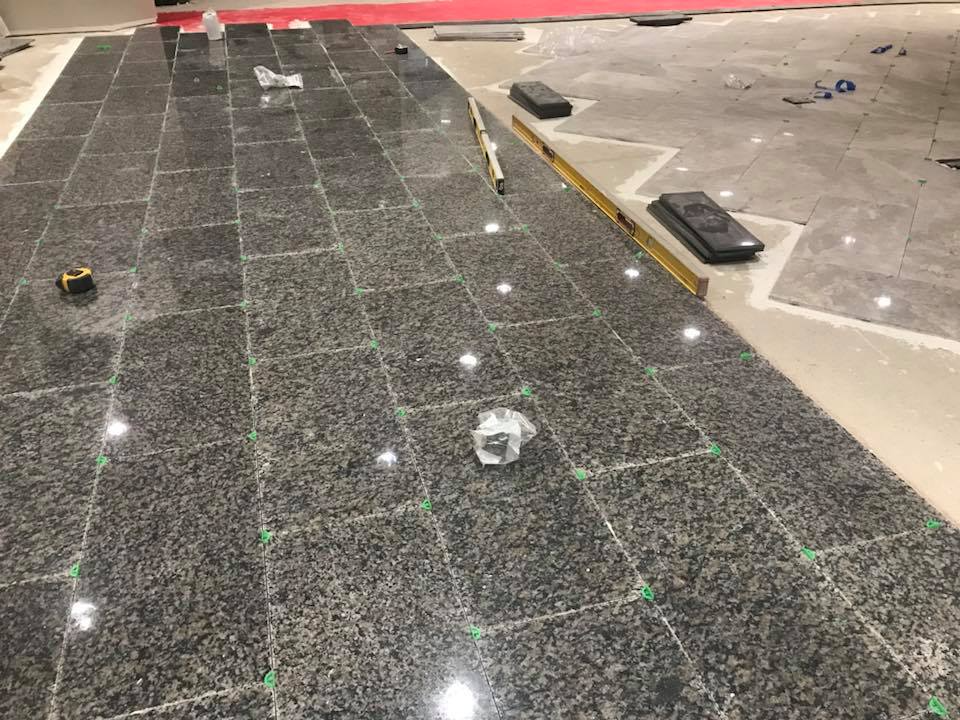 Floor tiling in progress; dark granite tiles laid with spacers on a gray floor.