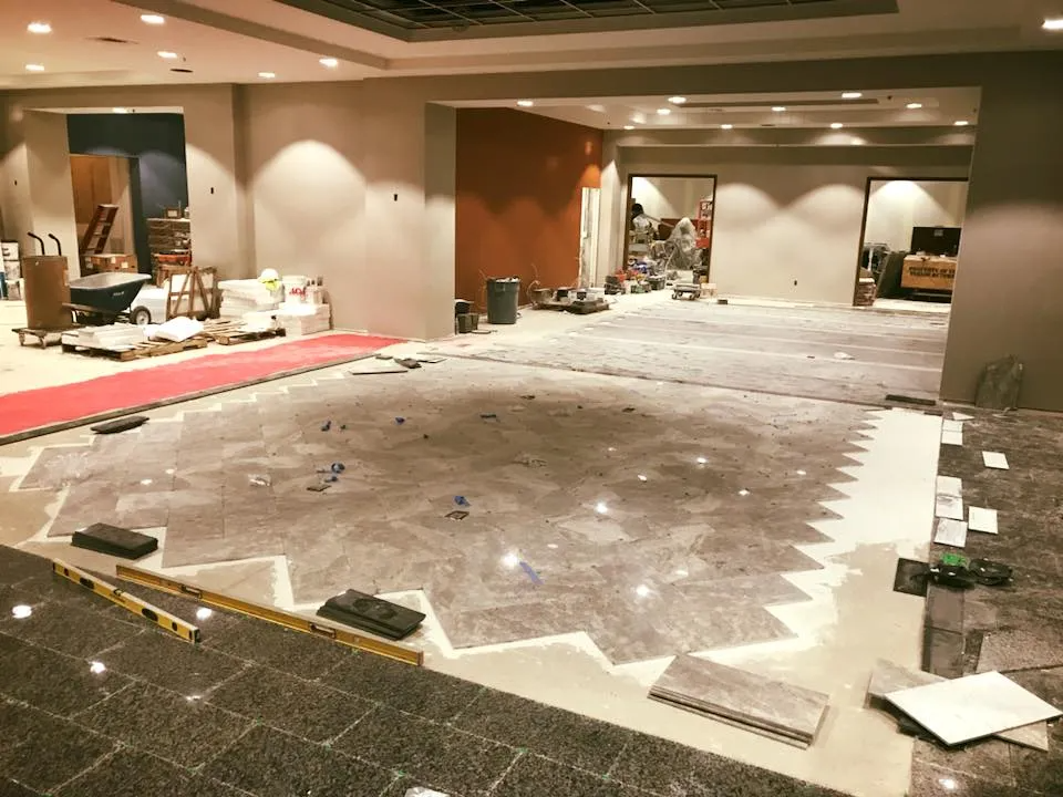 Room under renovation with partially tiled floor. Gray and orange walls, tools, and materials are visible.