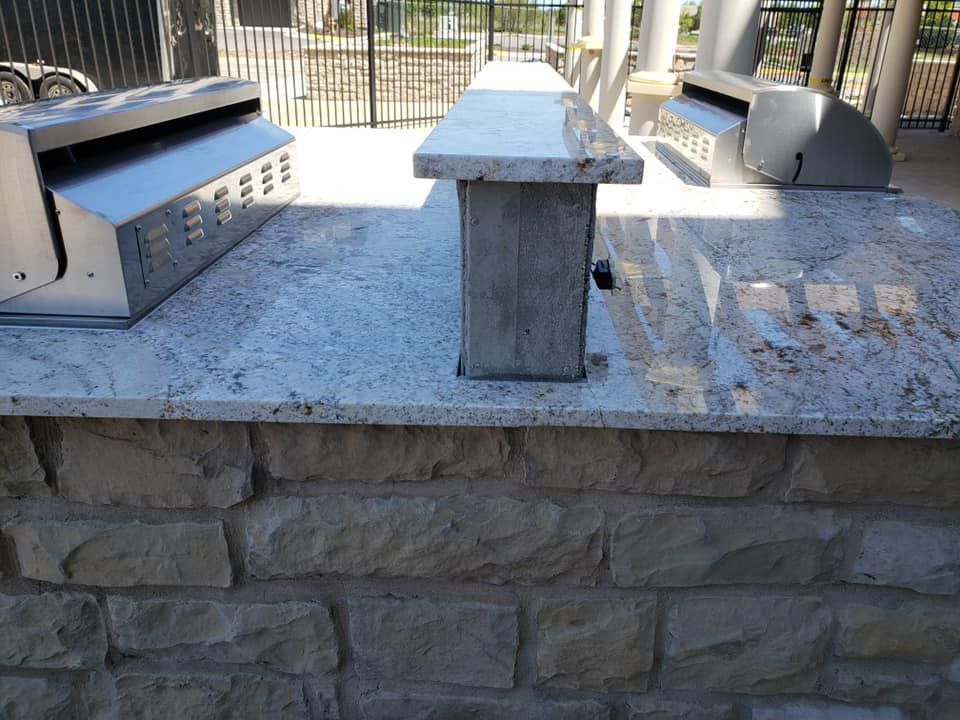 Outdoor kitchen with granite countertop, stone brick base, and stainless steel grills.
