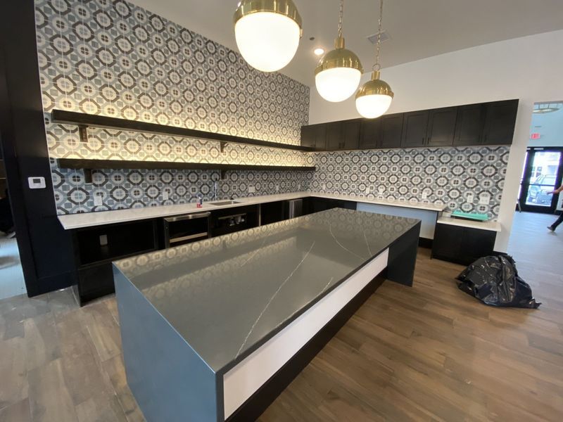 Modern kitchen with gray countertop island, patterned backsplash, black cabinets, wood floors, and pendant lights.
