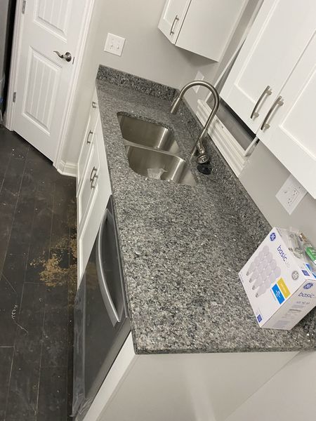 Kitchen counter with a double sink, granite countertop, white cabinets, and stainless steel dishwasher.