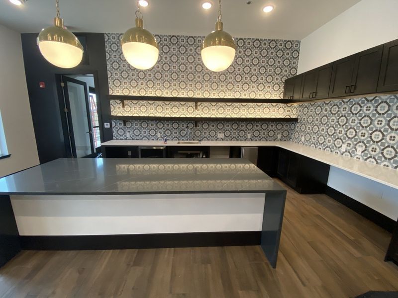 Modern kitchen with patterned backsplash, black cabinets, and island with pendant lights.