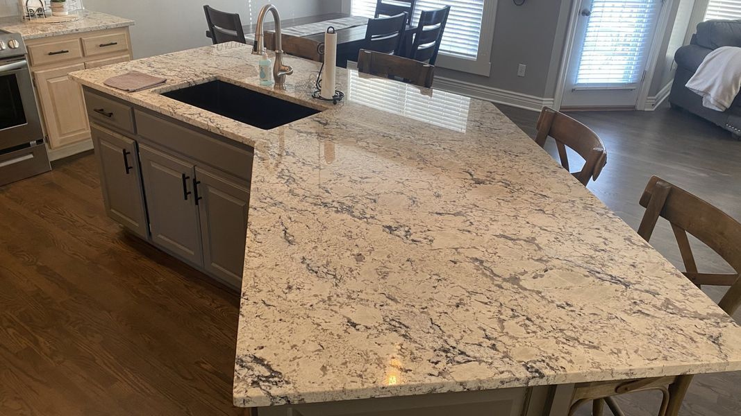 Kitchen island with light granite countertop, dark sink, and seating. Wooden floors and cabinets.