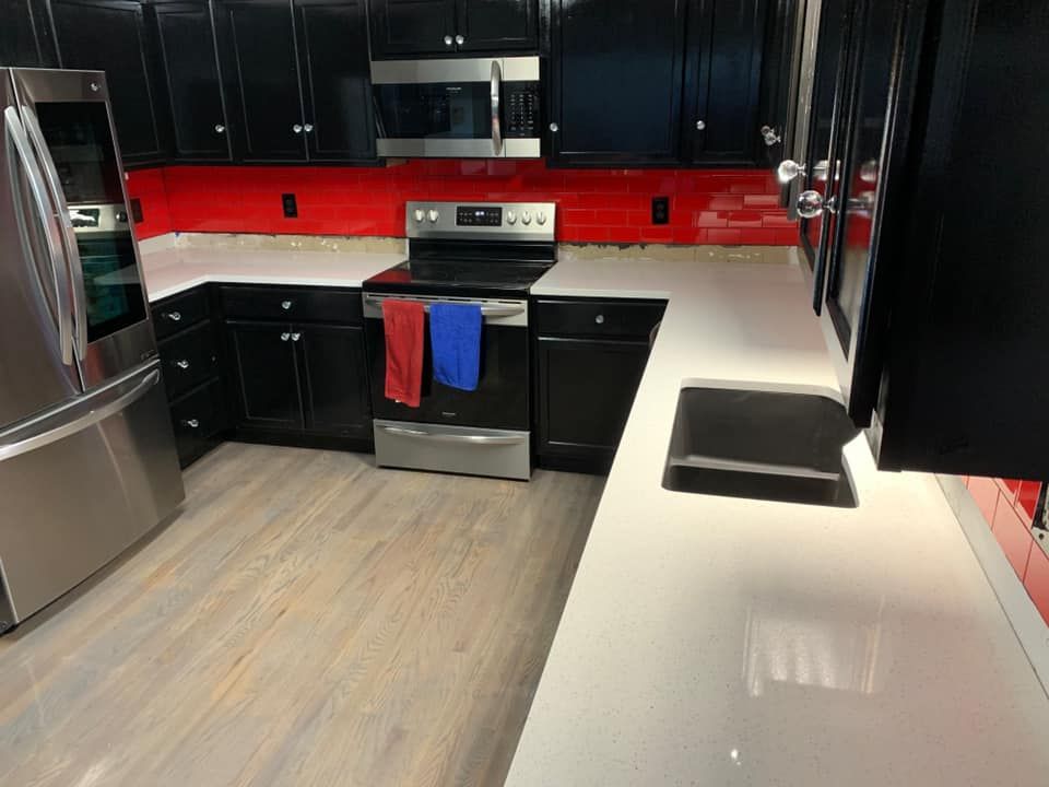 Modern kitchen with black cabinets, red backsplash, stainless steel appliances, and white countertops.