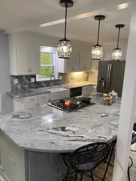 Modern kitchen with island, gray countertops, white cabinets, and three pendant lights.