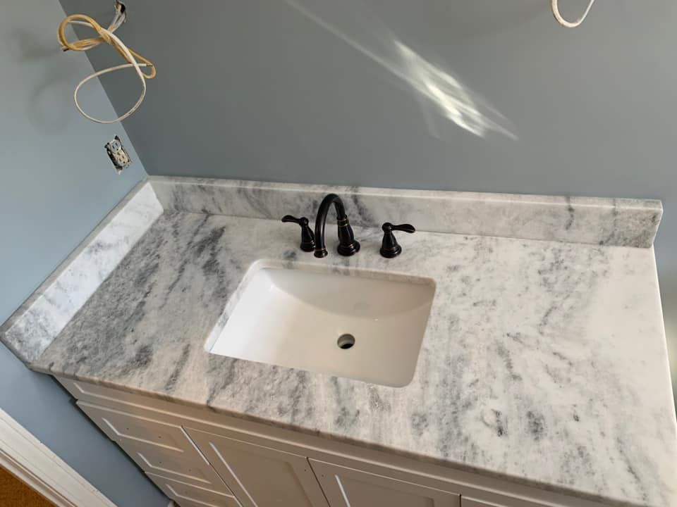 White marble countertop with sink, black faucet, and white cabinet in a bathroom.
