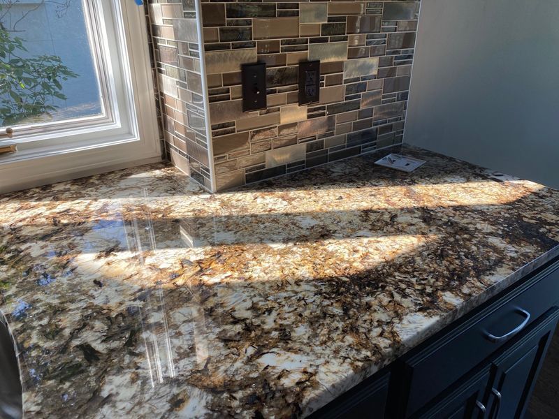 Granite countertop with brown and tan swirls, under a mosaic tile backsplash and window.