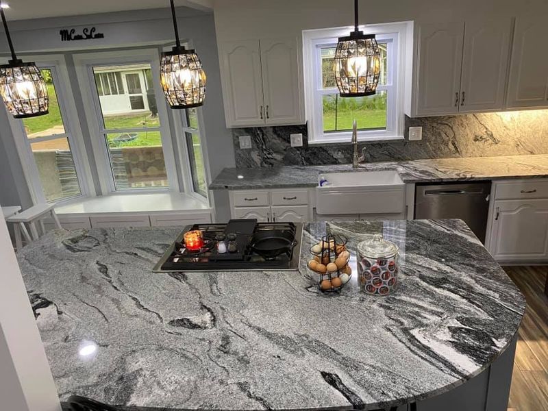 Kitchen with granite countertops, white cabinets, and pendant lights. A cooktop is on the island.