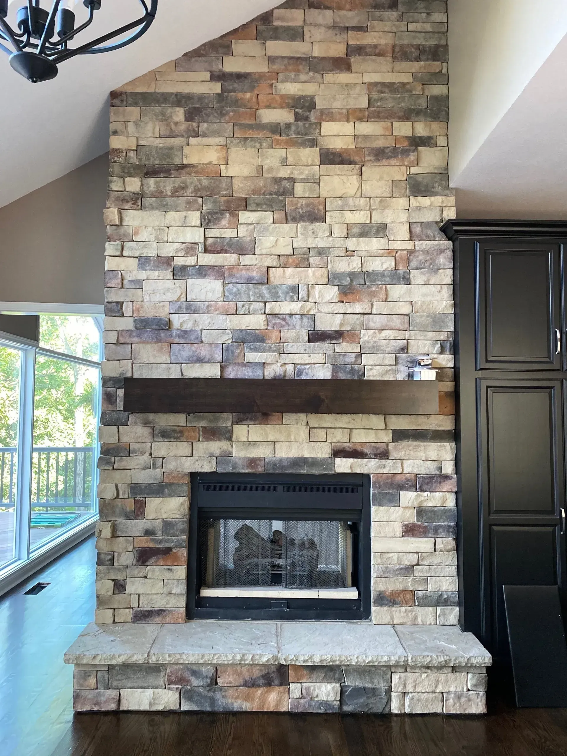 Stone fireplace with dark wood mantel, black cabinet to the right.
