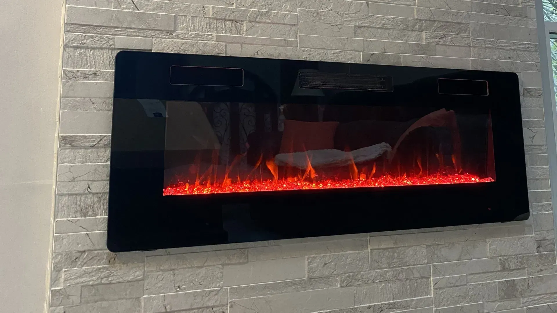 Black electric fireplace on a white stone wall, displaying orange flames.