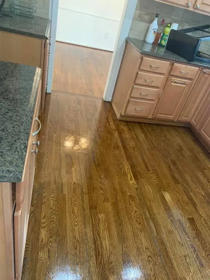 Wooden kitchen floor, light cabinets, and granite countertop. View into hallway with wooden flooring.