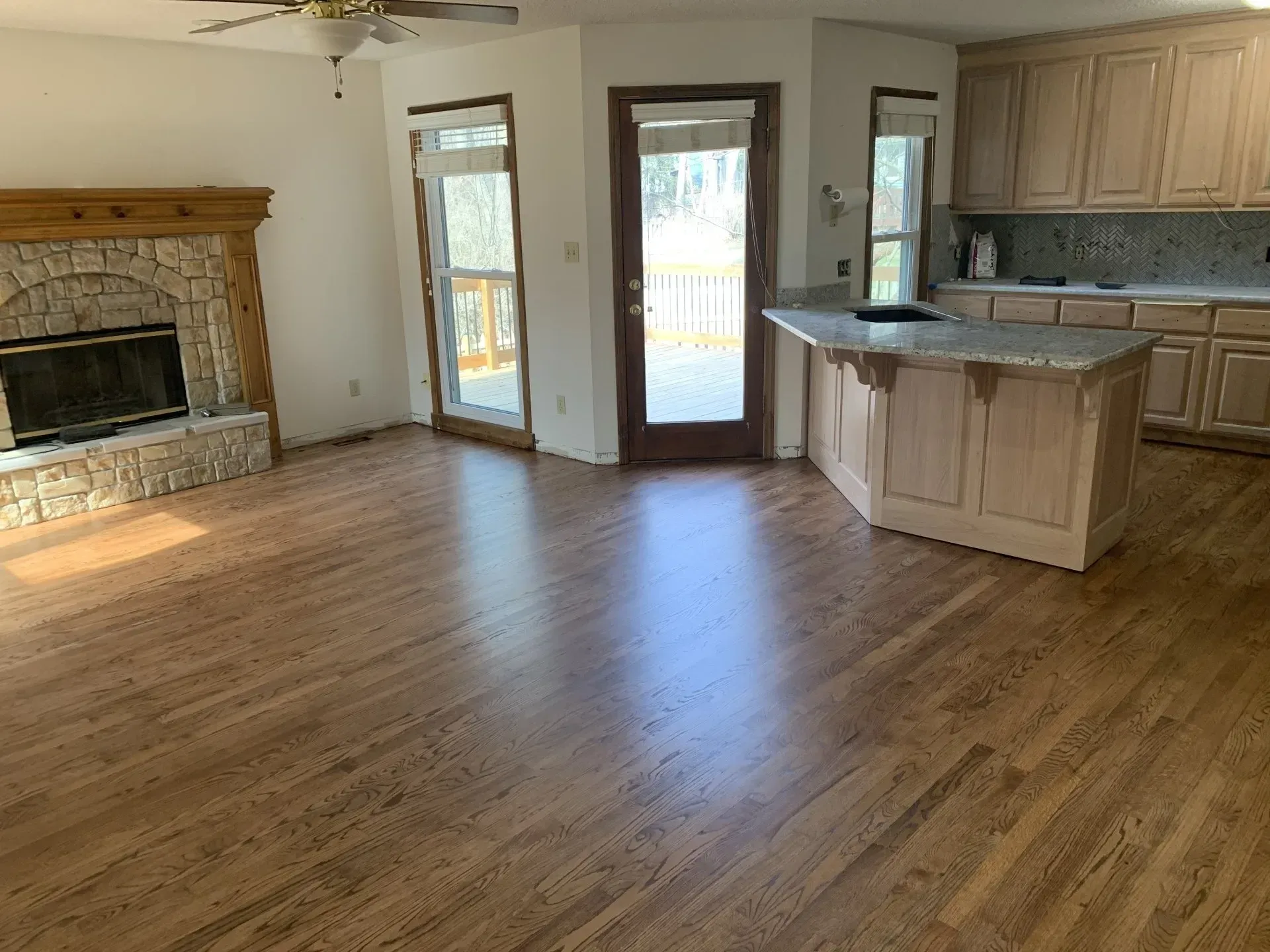 Living room with stone fireplace, wood floors, and kitchen with island.