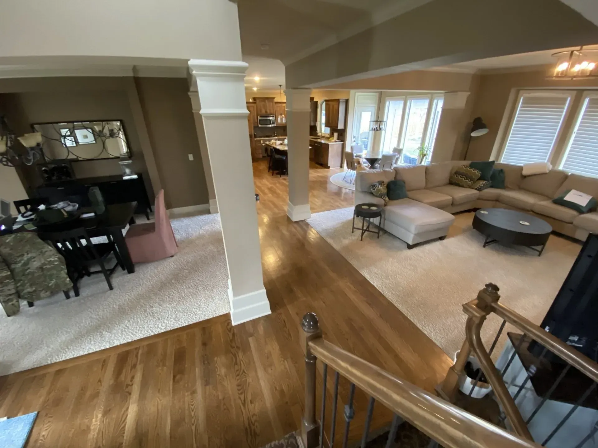 Hardwood floor leads to a living room with a sectional sofa and dining room with a table.