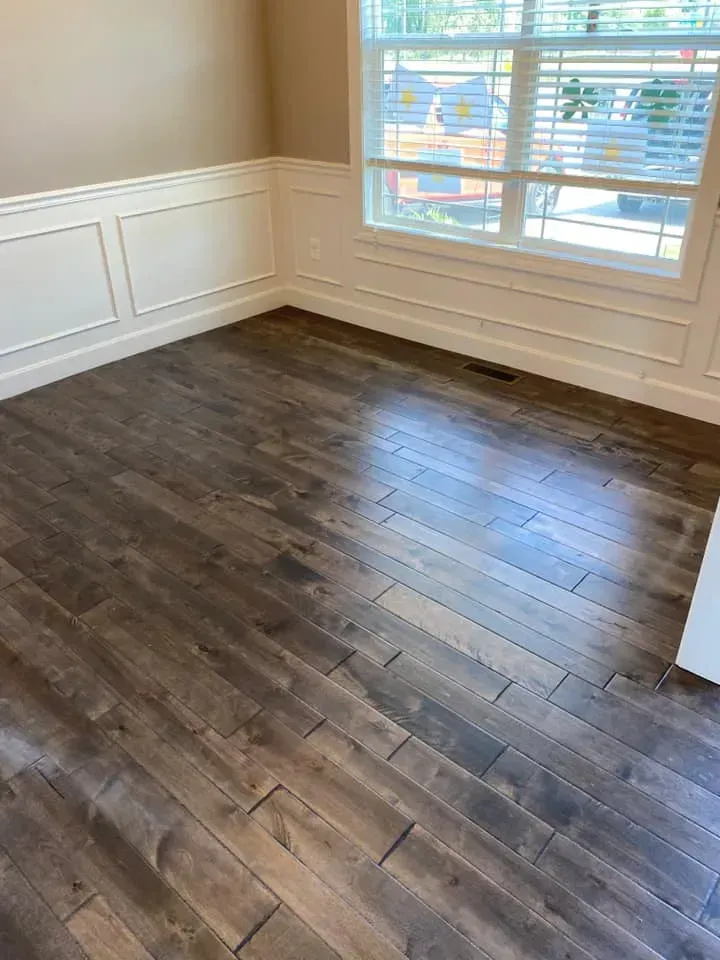 Dark wooden floor in a room with white wainscoting and a window with natural light.