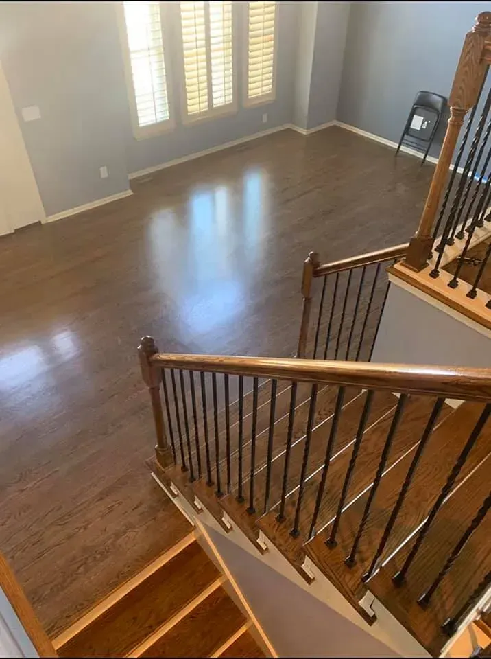 View from top of stairs into a room with hardwood floors and windows, dark wood banister and railings.