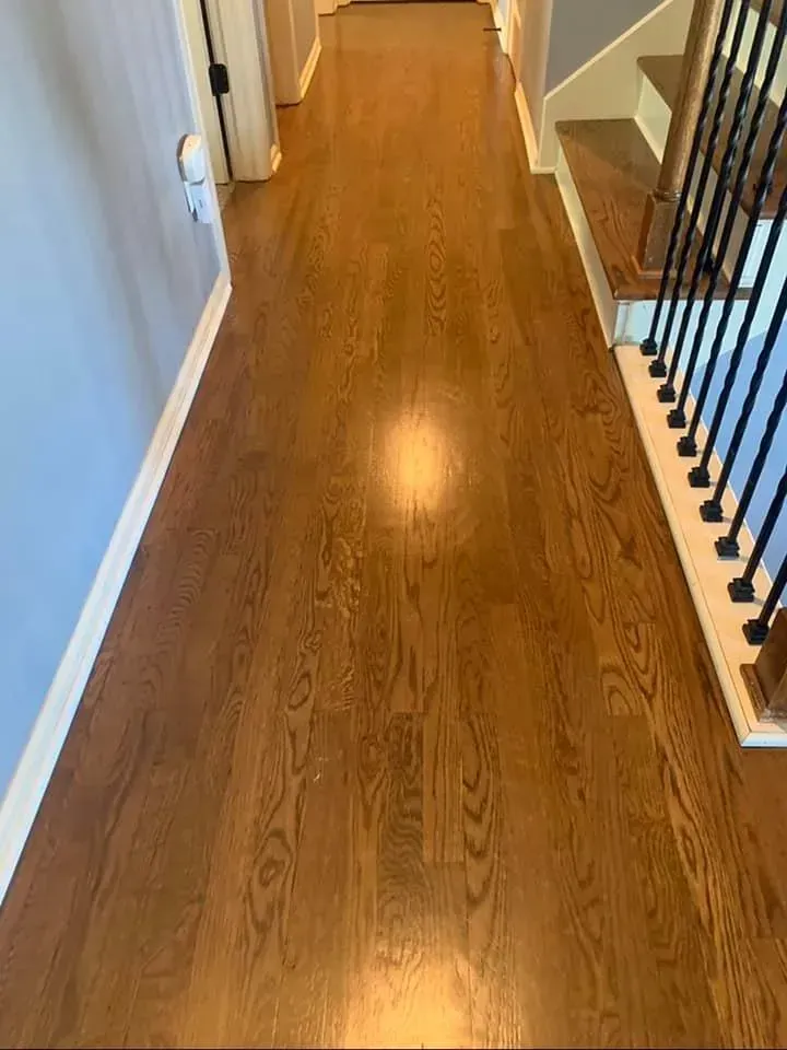Hardwood floor hallway leading to a staircase, with brown flooring and a light source in the center.