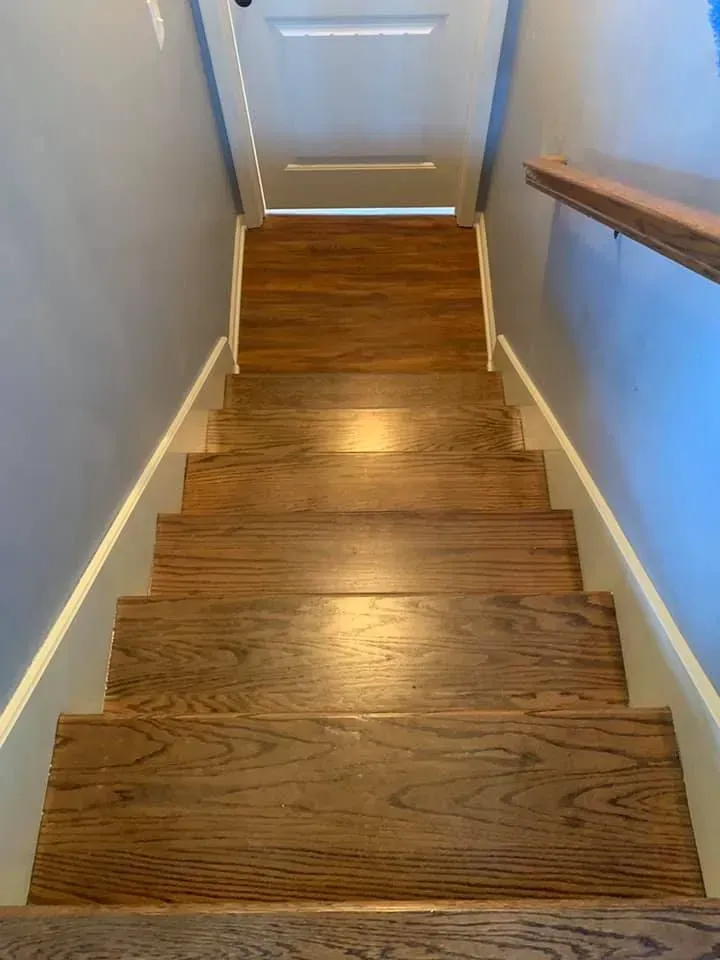 Wooden staircase leading upwards, with blue walls and a wooden handrail on the right.