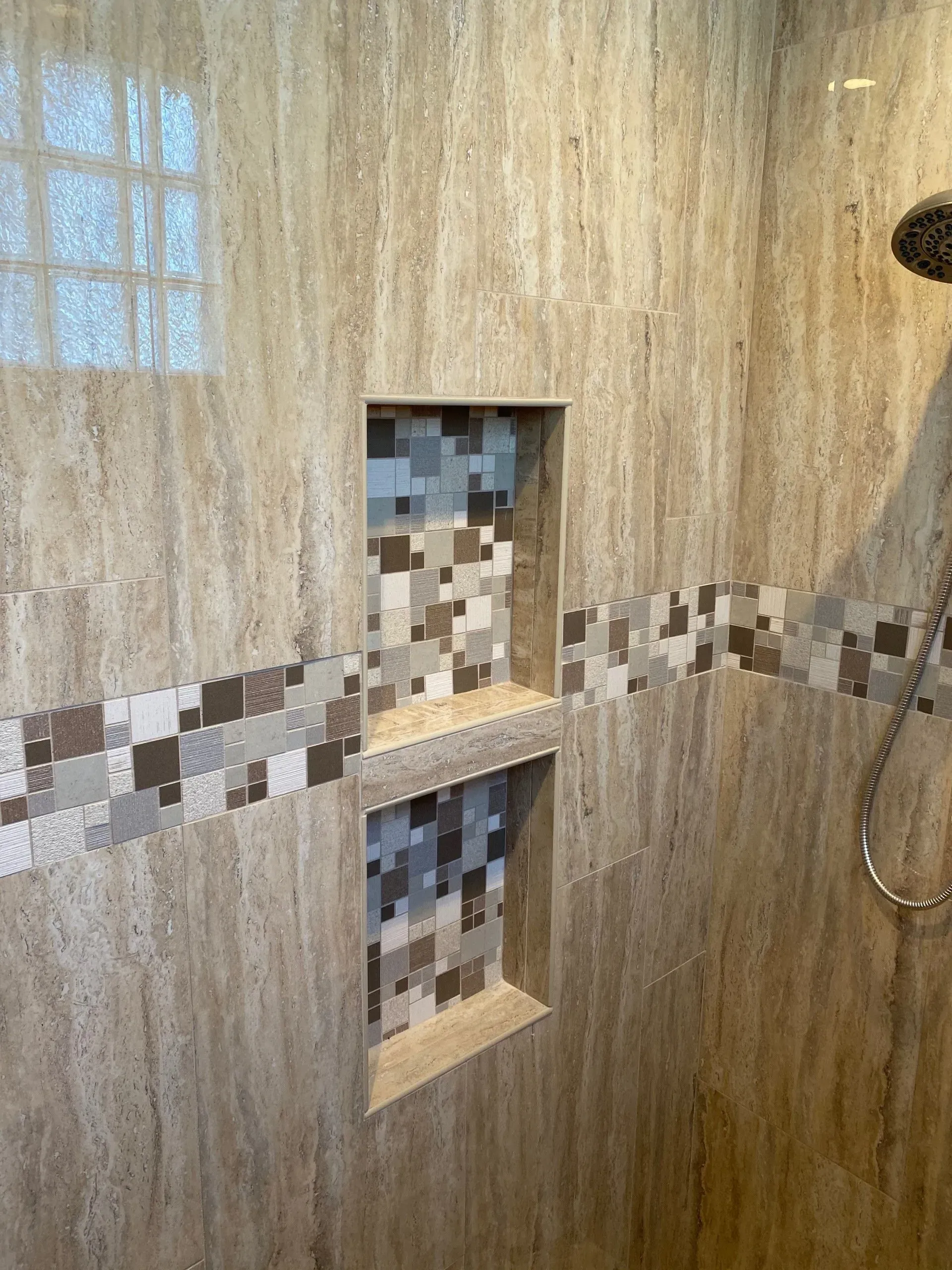 Shower with beige tile and mosaic accent, two built-in storage niches.