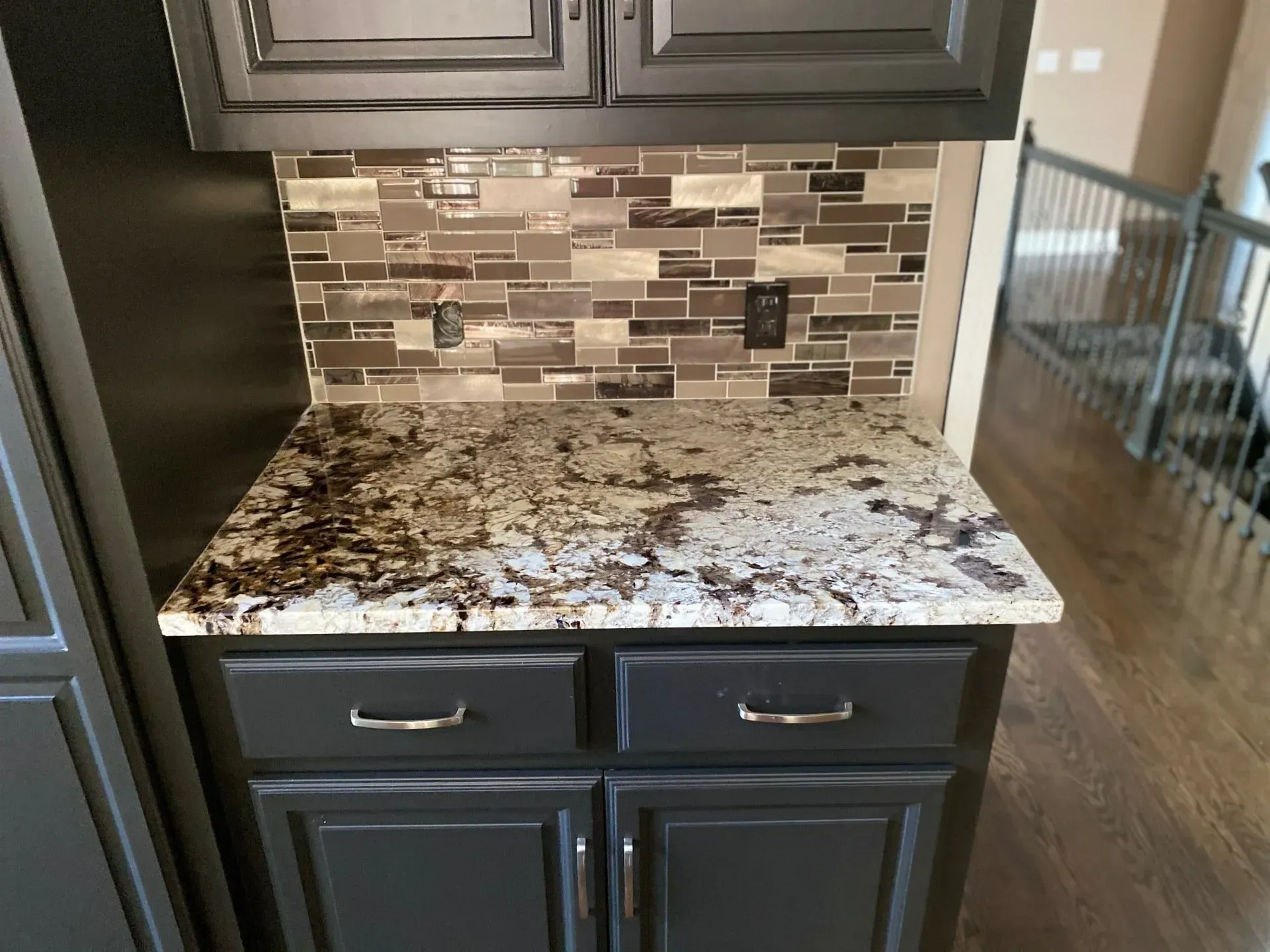 Kitchen countertop with granite and mosaic tile backsplash, black cabinets, and recessed lighting.