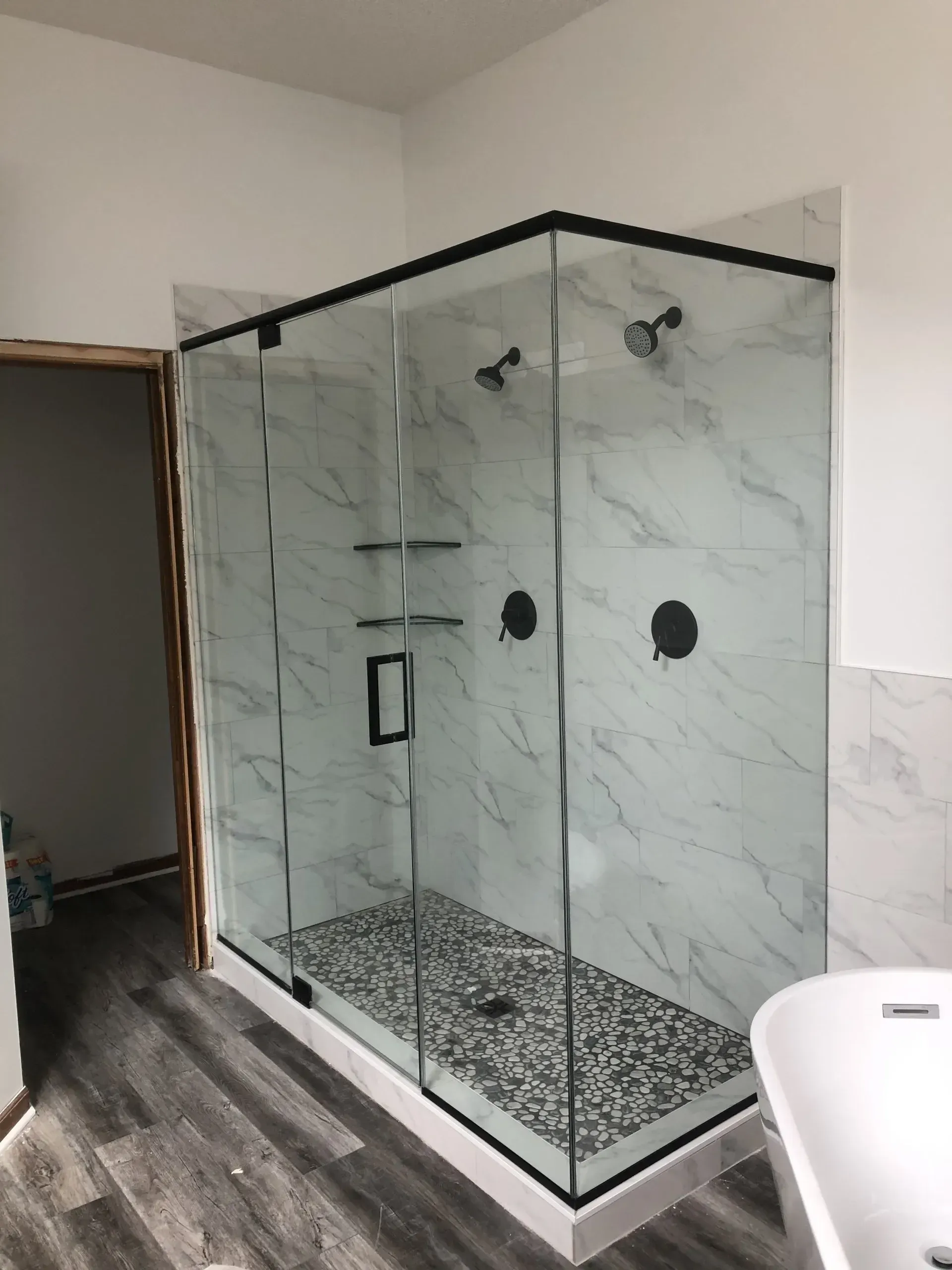 Modern glass shower enclosure with black trim, marble tile, and pebble floor.